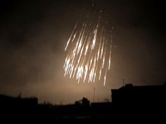 fireworks are lit up in the dark sky above some buildings and rooftops at night