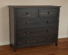 a wooden dresser sitting on top of a hard wood floor next to a white wall