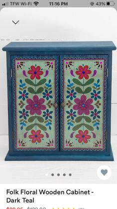 a blue cabinet with colorful flowers painted on it's doors and the words folk floral wooden cabinet - dark teal