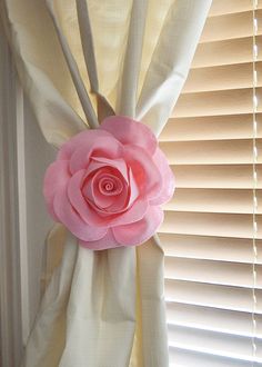 a pink flower is hanging on the side of a window with white curtains behind it