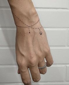 a person's hand with a small tattoo on the left wrist and a chain around it