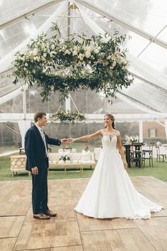 a bride and groom hold hands while standing on a dance floor in a tented area