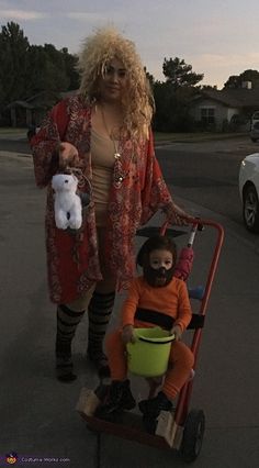 a woman in an orange shirt is pushing a wagon with a doll on it