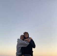 two people hugging each other while standing on top of a hill with the sky in the background