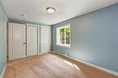 an empty room with blue walls and white doors, carpeted floor, and two windows