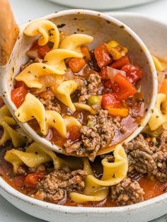 a white bowl filled with pasta and meat soup next to a piece of bread on the side