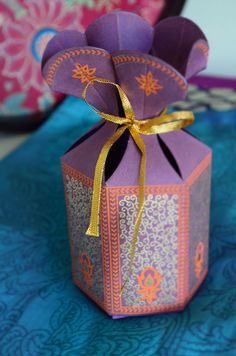 an origami box that has been folded and tied with a gold ribbon on top