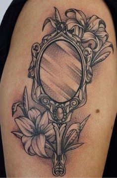 a woman's arm with a mirror and flowers tattoo on the back of her shoulder