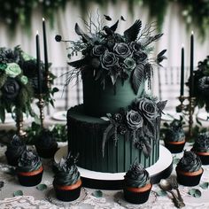 a green wedding cake surrounded by cupcakes and greenery with candles in the background