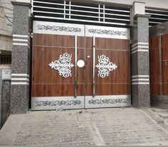 two large wooden doors with intricate designs on the front and side of a gray building