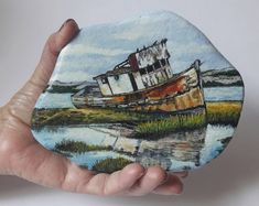 a hand holding up a painted rock with a boat on it