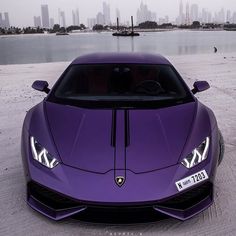 a purple sports car parked in front of a large body of water with buildings in the background