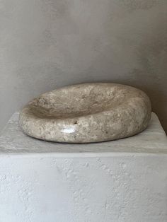 a large stone bowl sitting on top of a white pedestal in front of a wall