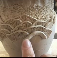 a hand is touching the bottom of a vase with white glazes on it