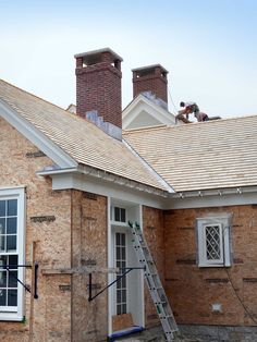 two men working on the roof of a brick house with a ladder in front of it