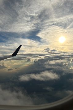 the wing of an airplane as it flies in the sky with clouds and sun behind