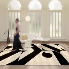 a woman walking across a living room with black and white rugs