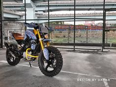 a blue and yellow motorcycle parked in a parking lot next to a fence with graffiti on it