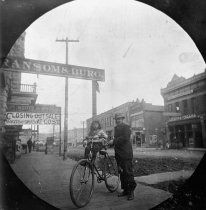 an old black and white photo of a man on a bike next to a street sign