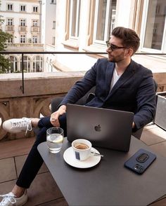 a man sitting at a table with a laptop computer on his lap and a cup of coffee in front of him