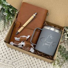 an open box containing a mug, notebook and pen