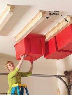 a woman standing on a step ladder holding two red bins above her head, with the bottom planks removed