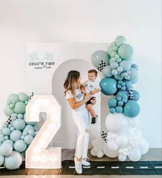 a woman holding a small child in front of balloons and the number twenty two sign