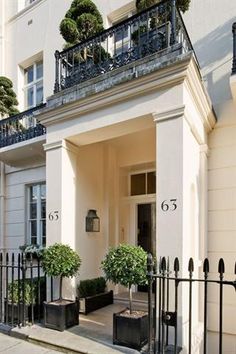 a white house with black iron railings and potted plants on the front door