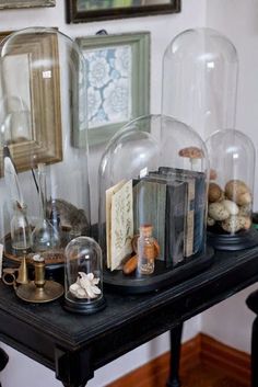 there are many cloches and books under glass dome covers on the black table