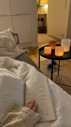 a person laying in bed reading a book with candles on the side table next to them