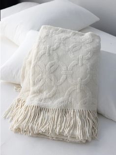 a white blanket sitting on top of a bed covered in pillows and blankets with fringes