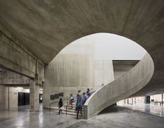 several people are walking up and down the stairs in an open area with concrete walls