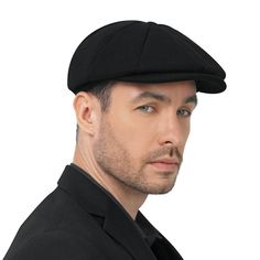 a man wearing a black suit and hat with no hair is looking at the camera