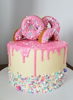 a pink frosted cake with sprinkles and donuts sitting on top