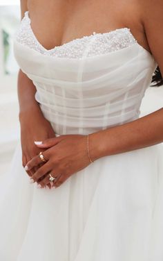 a woman in a white dress is holding her hand on her hip and wearing gold rings