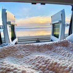 the inside of a vehicle looking out at an ocean and beach with two beds in it