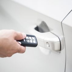 a hand is holding a remote control to a car door handle and pressing the button