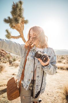 a woman taking a photo with her camera in front of a joshua tree and desert landscape