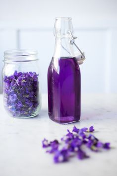 purple flowers sit in front of a glass bottle filled with water and lavender flakes