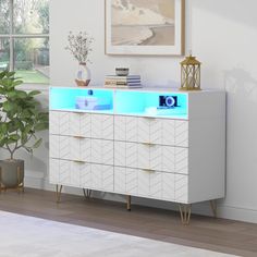 a white dresser with blue lights on it in a room next to a potted plant