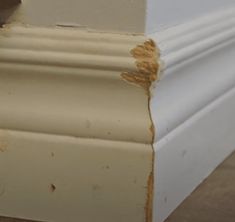 the corner of a white wall with some brown paint on it's edges and an orange piece of wood sticking out from underneath