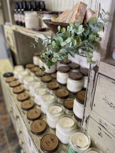 many jars are lined up on the shelf with candles in them and some green leaves