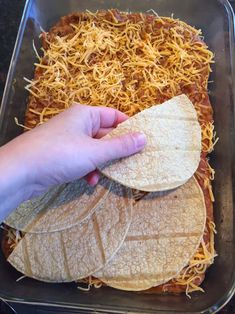 someone is placing tortilla shells on top of shredded cheese in a casserole dish