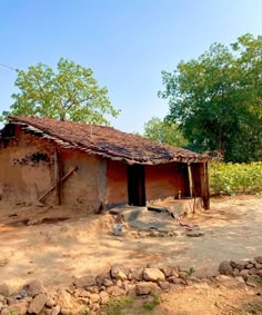 an old adobe house sits in the middle of a dirt field with rocks and trees around it