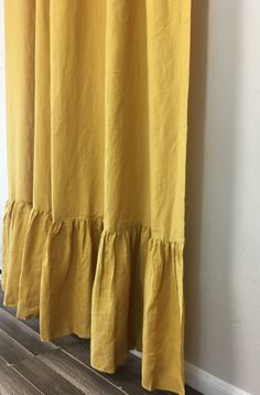 a yellow curtain hanging on the side of a wall next to a wooden floor and white walls