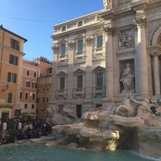 a group of people standing in front of a building next to a fountain with statues on it