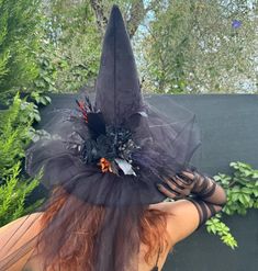 a woman wearing a black witch hat with feathers and flowers on it's head