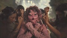 a woman with her face painted pink and surrounded by other women holding their hands in the air