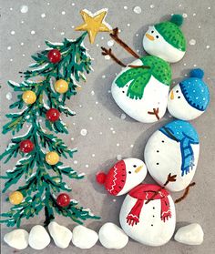 two snowmen with hats and scarfs next to a christmas tree made out of rocks