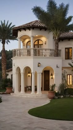 a large white house with palm trees in the front yard and lights on it's balconies